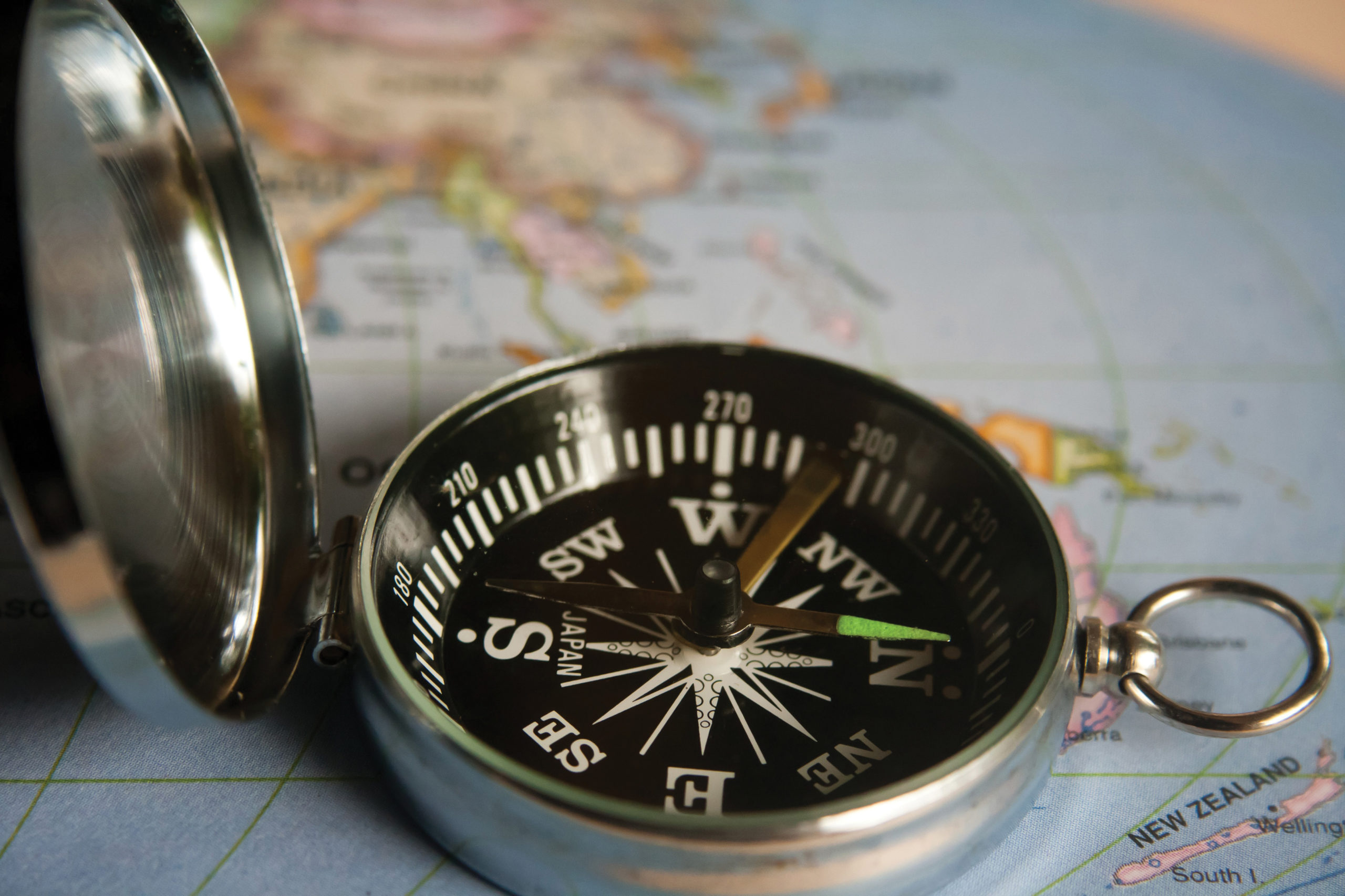 A silver compass, lid open, lying on a map